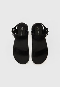 Sandales noires au design plat, dotées de straps en velcro ajustables et d'une semelle en caoutchouc lisse. Style simple et minimaliste.