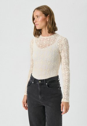 Off-white lace lange mouw top met een gestructureerd bloemenpatroon, gecombineerd met zwarte denim jeans met hoge taille. Strakke, aangesloten silhouet.