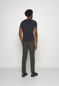 Schwarzes Sport-T-Shirt mit kurzen Ärmeln, kombiniert mit olivgrünen Slim-Fit-Hosen und schwarzen Sneakers, von hinten betrachtet.