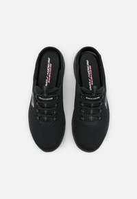 Svarta sportskor med ovandel i mesh, med en slip-on design, innersula i minneskum, elastiska skosnören och en logotyp på sidan.