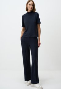 Top blu navy a maniche corte con scollatura alta abbinato a pantaloni larghi coordinati. Tessuto liscio, cuciture minime e tasche laterali.