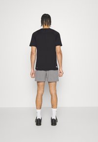 Svart kortärmad skjorta, grå shorts, med en mjuk textur och enkelt mönster. Svarta skor, vita ankle-strumpor. Neutral bakgrund.