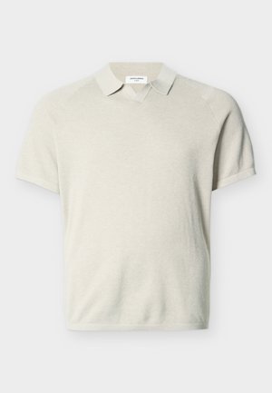 Lühikeste varrukatega beež kudumispolo särk krae ja peene tekstuurimustriga, laotatud valgele taustale.