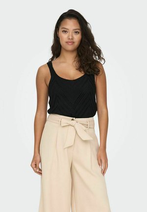 Débardeur en tricot noir avec un motif en chevrons, associé à un pantalon beige taille haute doté d'une ceinture nouée et d'une fermeture à boutons.