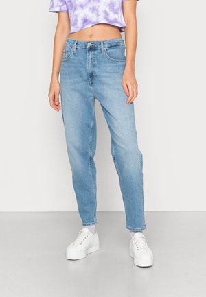 Jean slim bleu clair porté avec des baskets blanches à semelle compensée et un crop top tie-dye violet, visible de la moitié du torse jusqu'aux pieds.