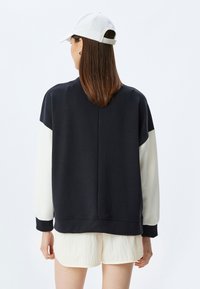 Svart och krämfärgad sweatshirth med avslappnad passform, ribbade ärmslut och rund halsringning. Mjuk tygstruktur, minimalistisk design och inga synliga logotyper.