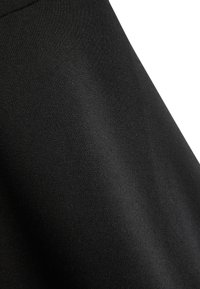 Primo piano di tessuto nero liscio e tessuto stretto che mostra la texture e lievi pieghe su uno sfondo bianco diagonale.