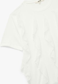 Camiseta blanca de manga corta con volantes en capas en el frente. Fabricada con tejido suave, tiene un cuello redondo y un corte relajado.