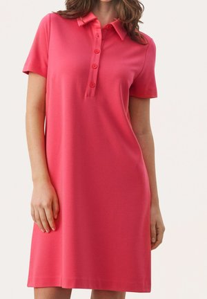 Femme portant une robe polo corail rose à manches courtes, longueur genou, avec un col et quatre boutons sur le devant.