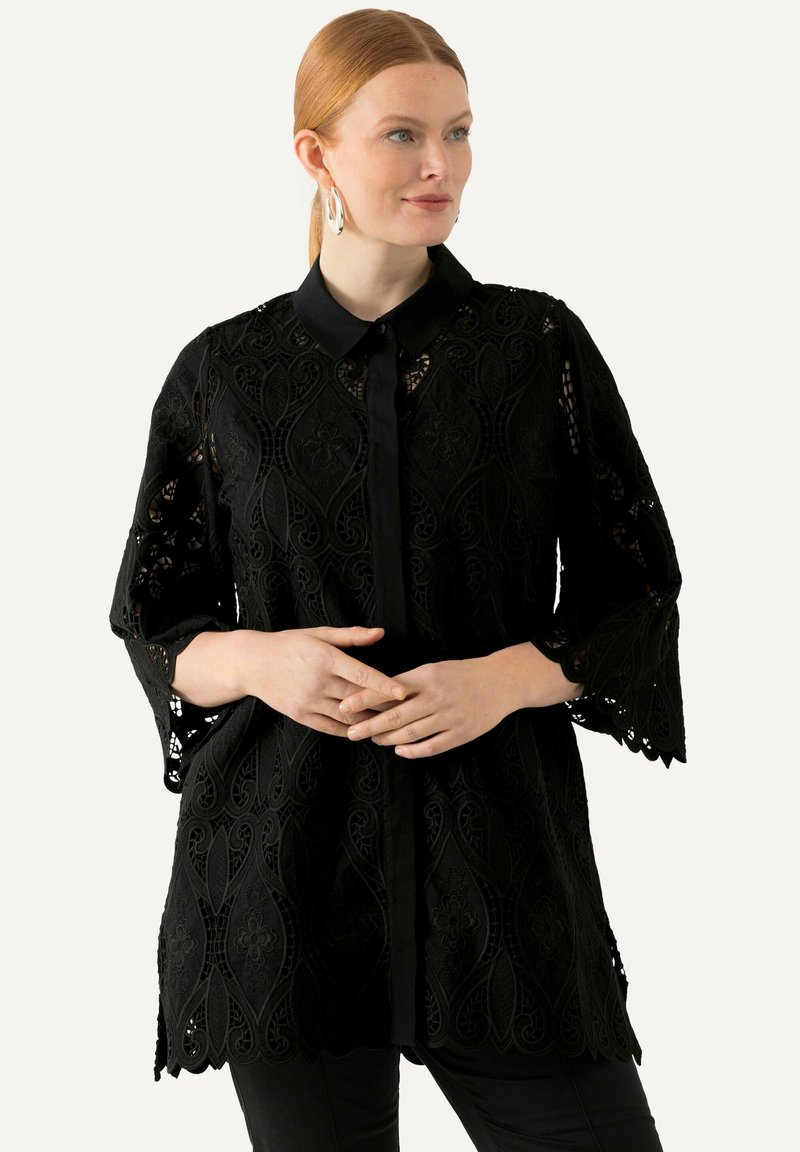 Blusa de encaje negro con cuello, mangas tres cuartos, intrincados patrones florales, dobladillo festoneado y cierre de botones en la parte delantera.