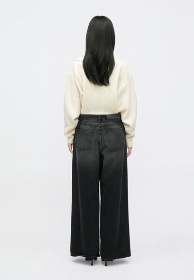 Široke črne denim sanje s gladko teksturo, visokim pasom in dvema zadnjima žepoma. Ujemajo jih smetanast, rebrast pleten jersey.