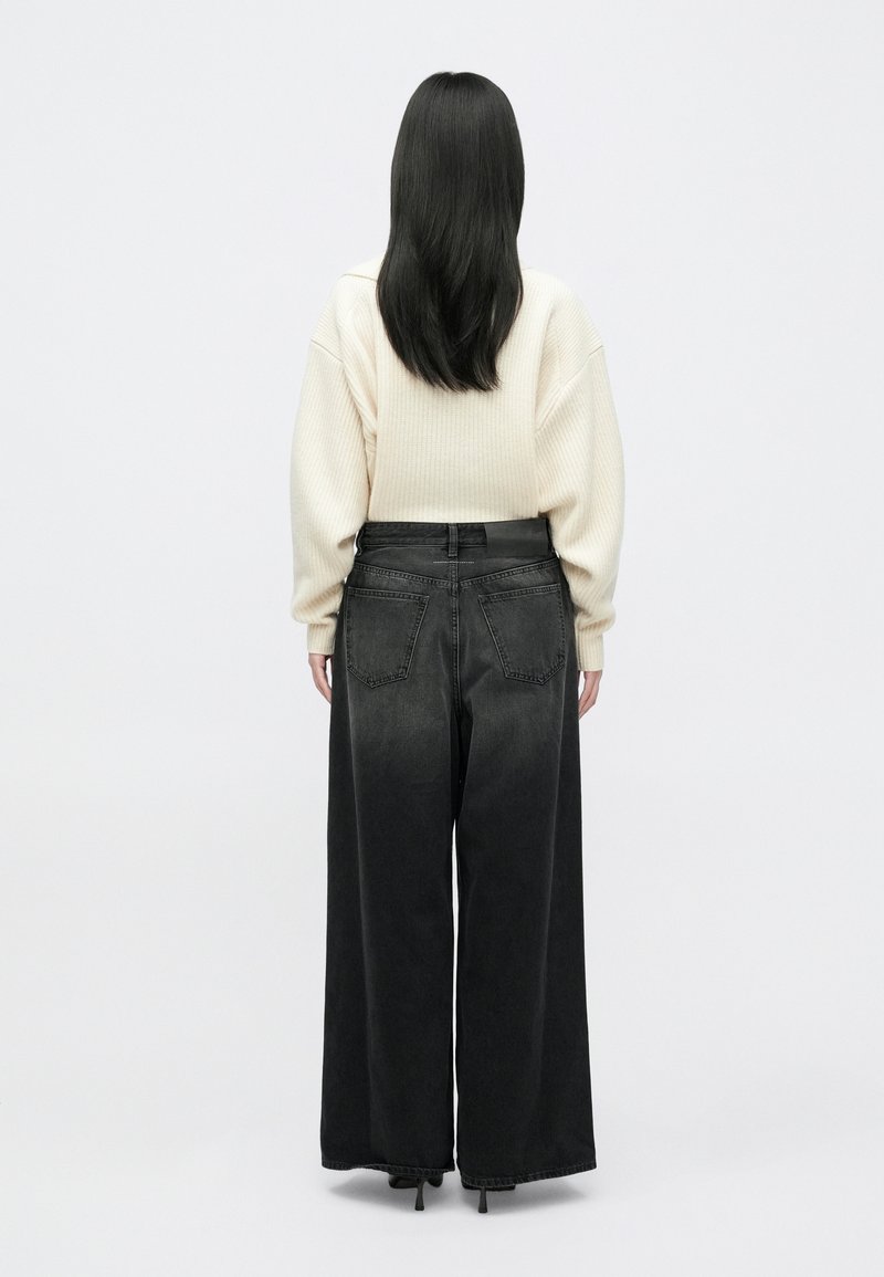 Zwarte denim jeans met brede pijpen, een soepele textuur, hoge taille en twee achterzakken. Gepaard met een crèmekleurige, geribbelde trui.
