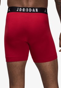 Boxeri din bumbac roșu, cu o croială strâmtă, având o talie neagră inscripționată cu „JORDAN” în litere albe și un mic logo decorativ.