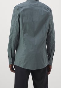 Camicia a maniche lunghe verde scuro, realizzata in tessuto leggero. Presenta una schiena dritta, polsini con bottoni e un design di colletto classico.