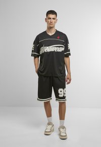Black sporty outfit featuring a loose-fit jersey with "Streetwear" text and number 99, paired with matching shorts and light sneakers.