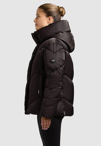 Black puffer jacket with a high collar and hood. Features quilted pattern, zippered pockets, and a logo patch on the sleeve.