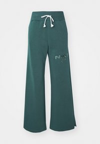 Tmavě zelené široké tepláky s bílým šňůrkovým stahováním a vyšitým logem Nike na horní levé noze.