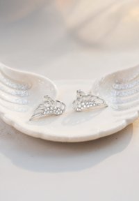 Silverörhängen med en delikat bladdesign, prydda med små, gnistrande stenar, visade på en vit skaldjursformad tallrik.