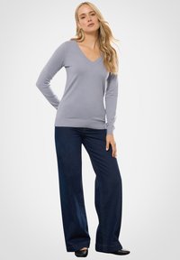 Lichtgrijze V-halstrui in een zachte brei, gecombineerd met donkerblauwe wijde jeans. De outfit heeft een relaxte pasvorm en minimale details.