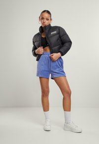 Svart puffjakke med logo, kombinert med lyseblå shorts og hvite joggesko. Utstyret har en avslappet passform og elastisk midje.
