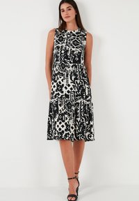 Black and white patterned dress with sleeveless design, tiered hem, and round neckline. Worn with black strappy heels.