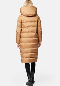Długi brązowy puchowy płaszcz z kapturem, z poziomymi przeszyciami, dopasowanym krojem i czarnymi botkami do kostek.