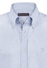 Camisa de botones azul claro con cuello estándar, logotipo de ave bordado y botones blancos sobre una tela suave y con textura.