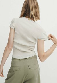 T-shirt côtelé beige clair à manches courtes, au design ajusté. Associé à un pantalon taille haute olive avec poches arrière.