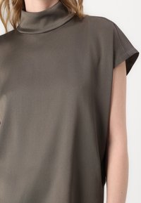 Blusa a maniche corte in tessuto grigio scuro con colletto alto, texture liscia e vestibilità comoda. Presenta spalle abbassate e design minimale.
