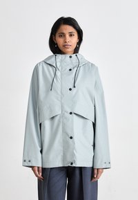 Light blue waterproof jacket with a hood, snap buttons, and side pockets. Features a layered design and loose-fitting silhouette.