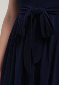 Robe bleu marine foncé avec ceinture en tissu nouée à la taille, montrant une jupe froncée et une partie d'un bras nu à côté.