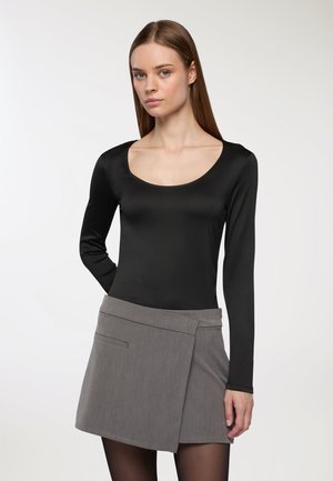 Body nero a maniche lunghe con scollo rotondo abbinato a una gonna avvolgente grigia, con un dettaglio di tasca frontale inclinata e una texture liscia.