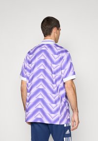 Camisa de manga corta con patrón geométrico púrpura y cuello y puños blancos, confeccionada en material ligero y con una textura suave.