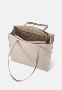 Beige tote taske lavet af tekstureret kunstlæder. Har lange håndtag, en lynlåslomme indeni og et præget logo på forsiden.