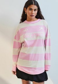 Üks suurte pikkade varrukatega sweatshirt, millel on triibuline pastelne roosa ja koorene värv, graafiline logo ja mugav lõike, valmistatud pehmest puuvillast materjalist.