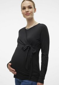 Maglietta premaman nera a maniche lunghe con design avvolgente e dettaglio di fiocco frontale, realizzata in tessuto morbido, abbinata a jeans blu.