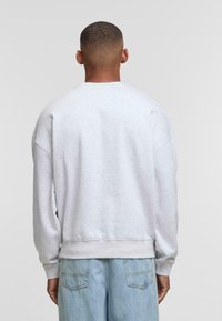 Hellegrauer Sweatshirt mit lässiger Passform, überhängenden Schultern und gerippten Bündchen. Weicher Frottee-Textur, getragen mit hellblauen, locker sitzenden Jeans.