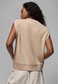 Ermeløs strikket topp i lys beige, med ribbestruktur, rund halslinje og en litt cropped nederkant.