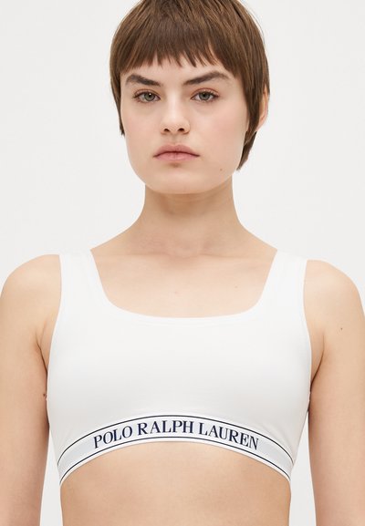 Vit ribbad bralette med breda axelremmar och fyrkantig halsringning. Har ett marinblått logoband med "POLO RALPH LAUREN" i nederkant. Slät textur.