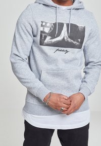 Felpa grigia con cappuccio realizzata in misto cotone, con grafica frontale di mani in posizione di preghiera e la scritta "pray" sotto. Include una tasca a marsupio.