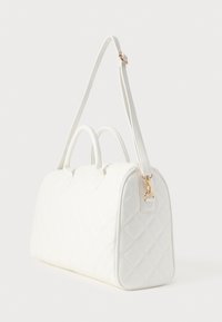 Λευκό καπιτονέ τσάντα με δομημένο σχέδιο, διπλές επάνω λαβές και αποσπώμενο λουράκι. Διαθέτει χρυσά μεταλλικά στοιχεία και λεία υφή.