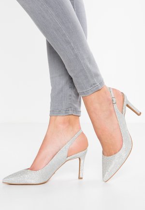 Zilveren slingbackhakken met een puntige neus, tekstuur metallic bovenkant en een dunne stilettohak, gecombineerd met grijze slim-fit spijkerbroeken.