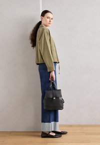 Olivgrön kort jacka, mörkblå vida jeans med fransad nederkant, svarta läderplatta skor och en svart läderryggsäck med spänne.