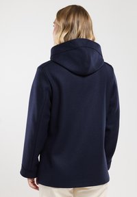 Cappotto blu marino con cappuccio e una texture liscia. Presenta un design semplice, una forma aderente e cuciture visibili lungo il cappuccio e le maniche.