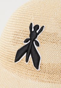 Beige cap med strukturert vevde mønster, med et svart brodert insektdesign omkranset i hvitt på forsiden.