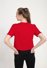 Red cotton t-shirt with short sleeves, rounded neck, and a relaxed fit, paired with fitted black jeans. Clear fabric texture visible.