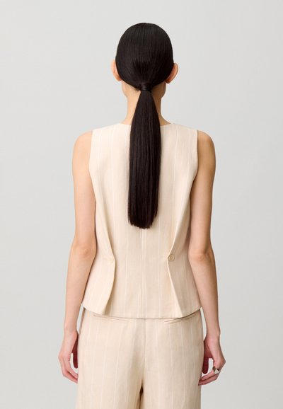 Top beige senza maniche con righe verticali, design aderente, due bottoni sul retro, abbinato a pantaloni a vita alta coordinati, tessuto dalla texture liscia.