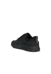 Scarpe sportive nere con una combinazione di materiali scamosciati e sintetici, punta arrotondata, suola testurizzata e un accento posteriore sottile.