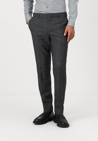 Pantalons gris à carreaux avec une coupe ajustée, présentant un devant plat, des passants de ceinture et un tissu texturé. Associés à des chaussures noires.