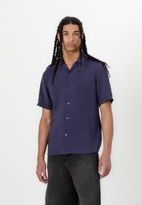 Marinblå kortærmet skjorte i let stof, med knaplukning fortil, afslappet krave og subtil glans. Bæres med mørk denim.
